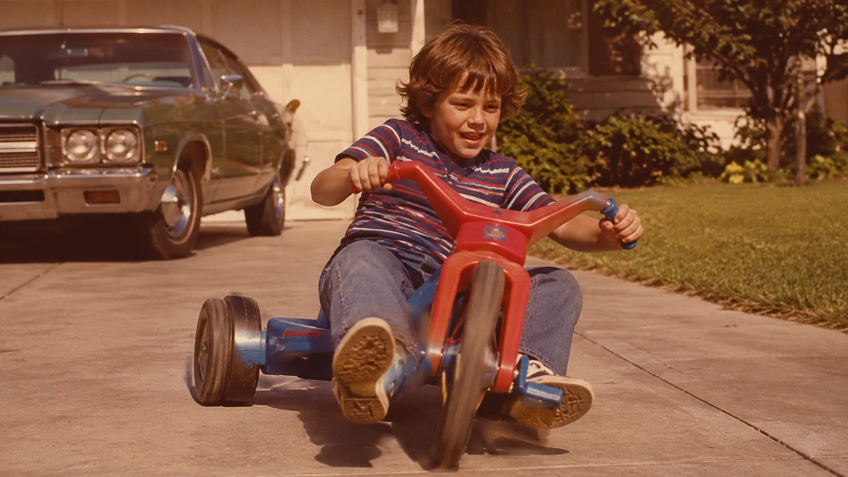 A child power-sliding a red-and-blue Big Wheel on a sunny 1970s driveway