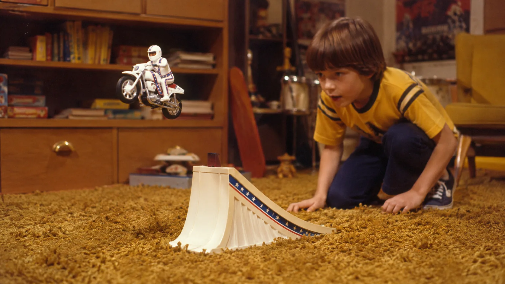 A child launching a motorcycle stunt rider over a plastic ramp on shag carpet