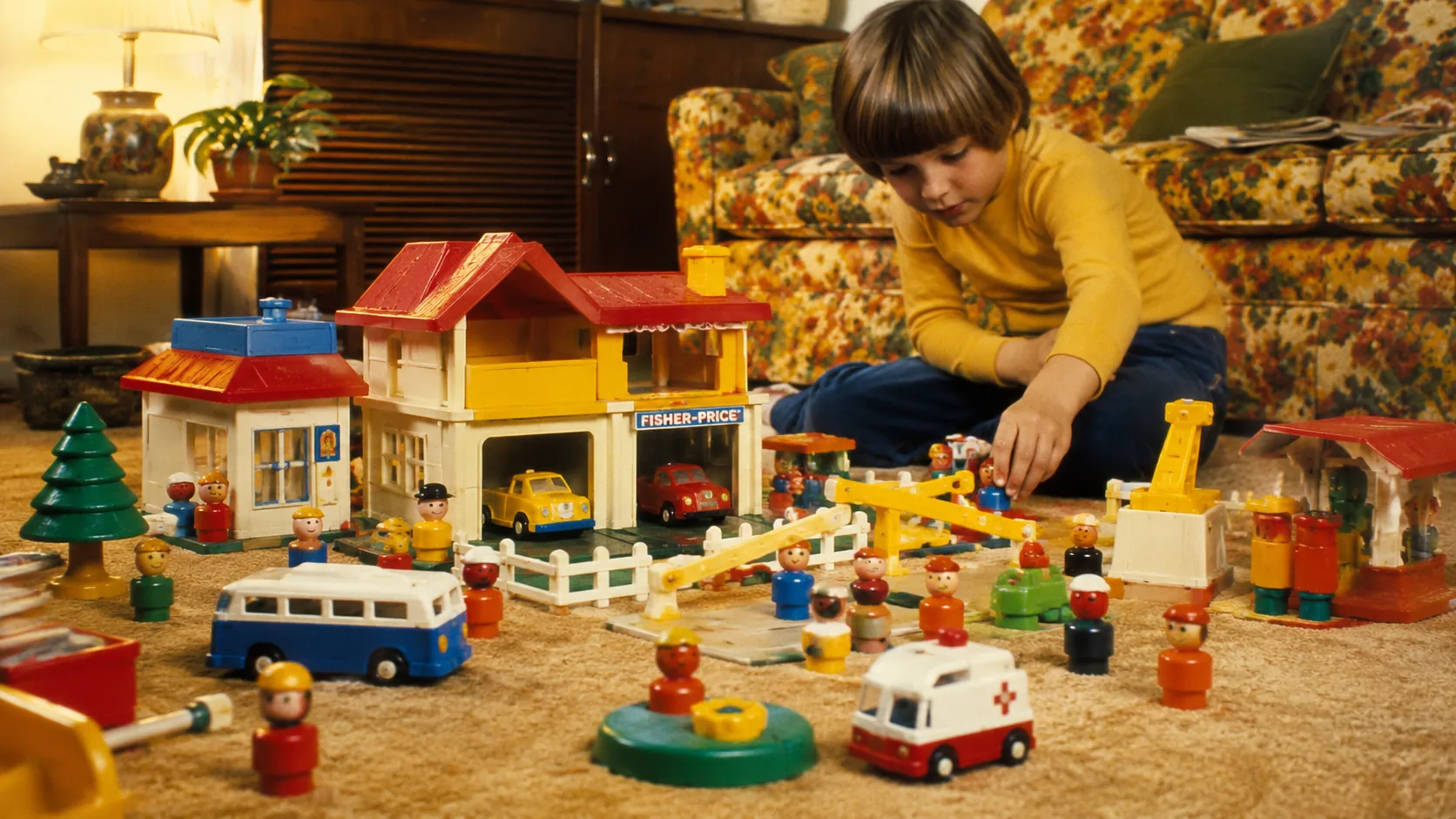 A child building a busy Fisher-Price Little People neighborhood with figures, vehicles, and playsets