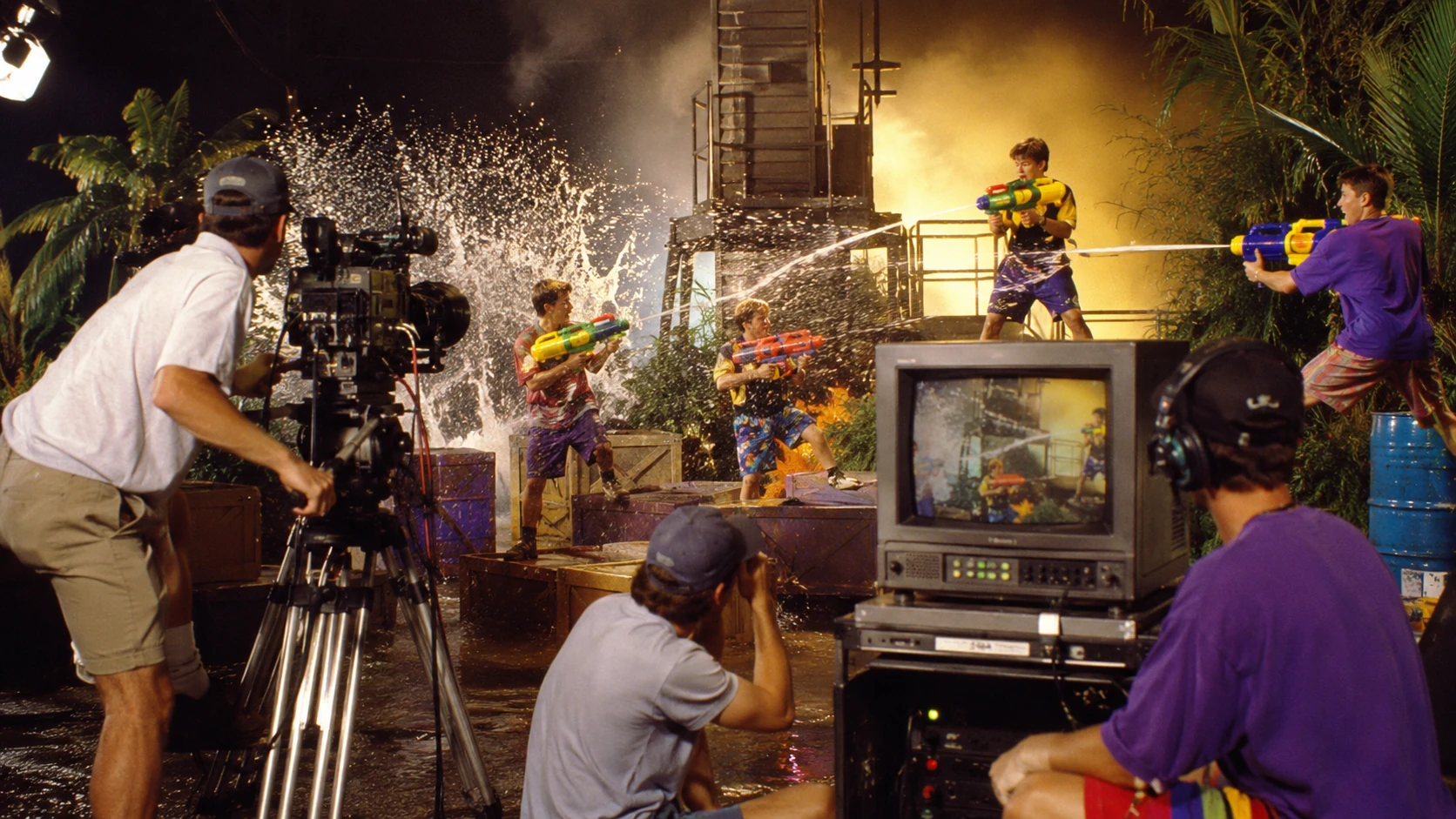 Behind-the-scenes 1990s-style water-blaster commercial shoot with cameras, CRT monitor and dramatic spray