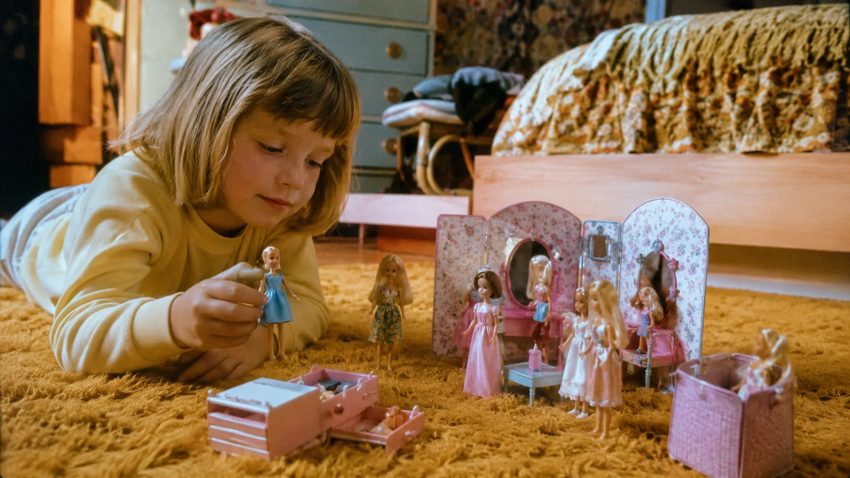 A child arranging small fashion dolls and accessories on a 1970s bedroom floor