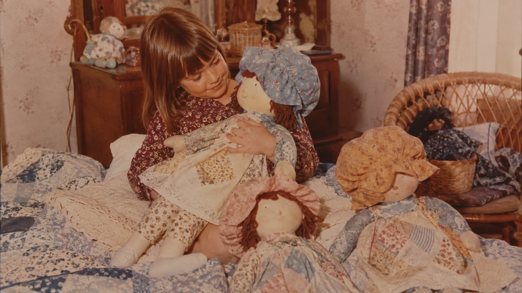 A child surrounded by soft Holly Hobbie-style dolls in a floral 1970s bedroom