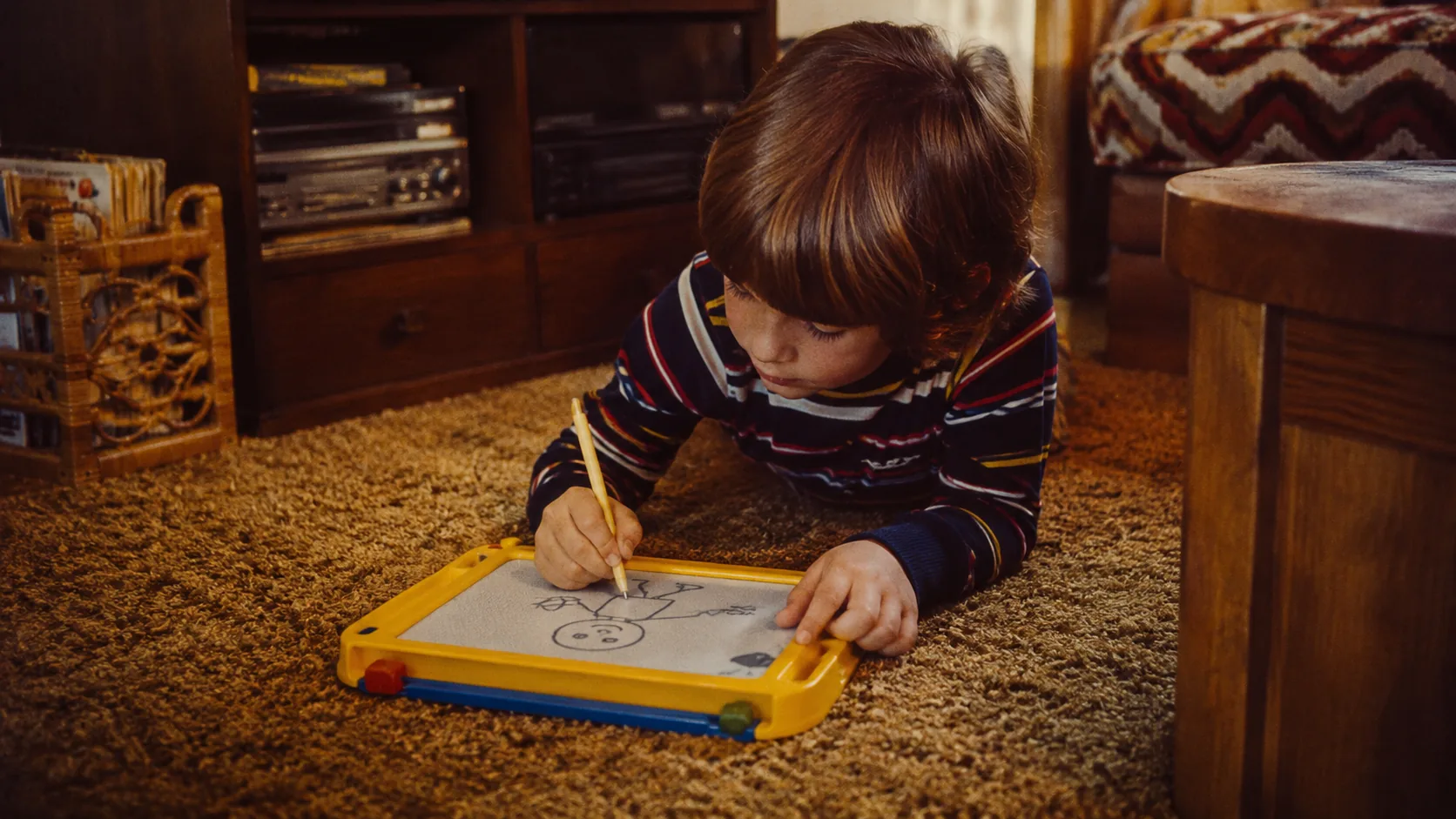 A child drawing on a magnetic sketch board on a 1970s shag carpet