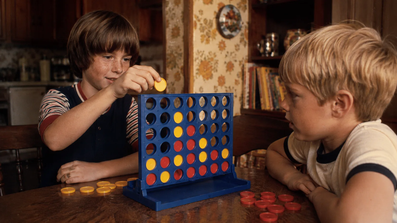 Two children playing Connect Four at a 1970s kitchen table