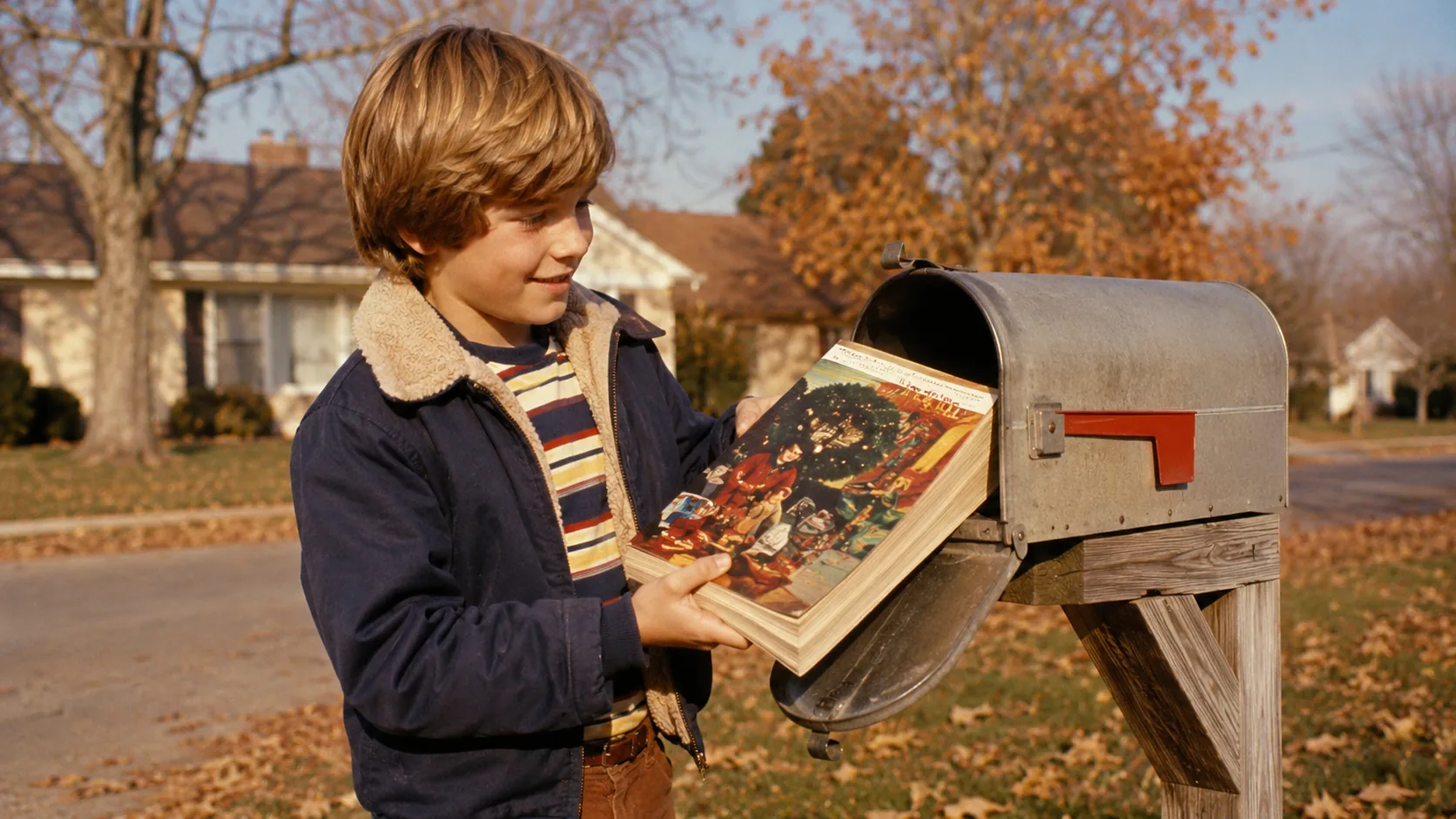 A child retrieving a thick Christmas catalog from a suburban mailbox in the 1970s