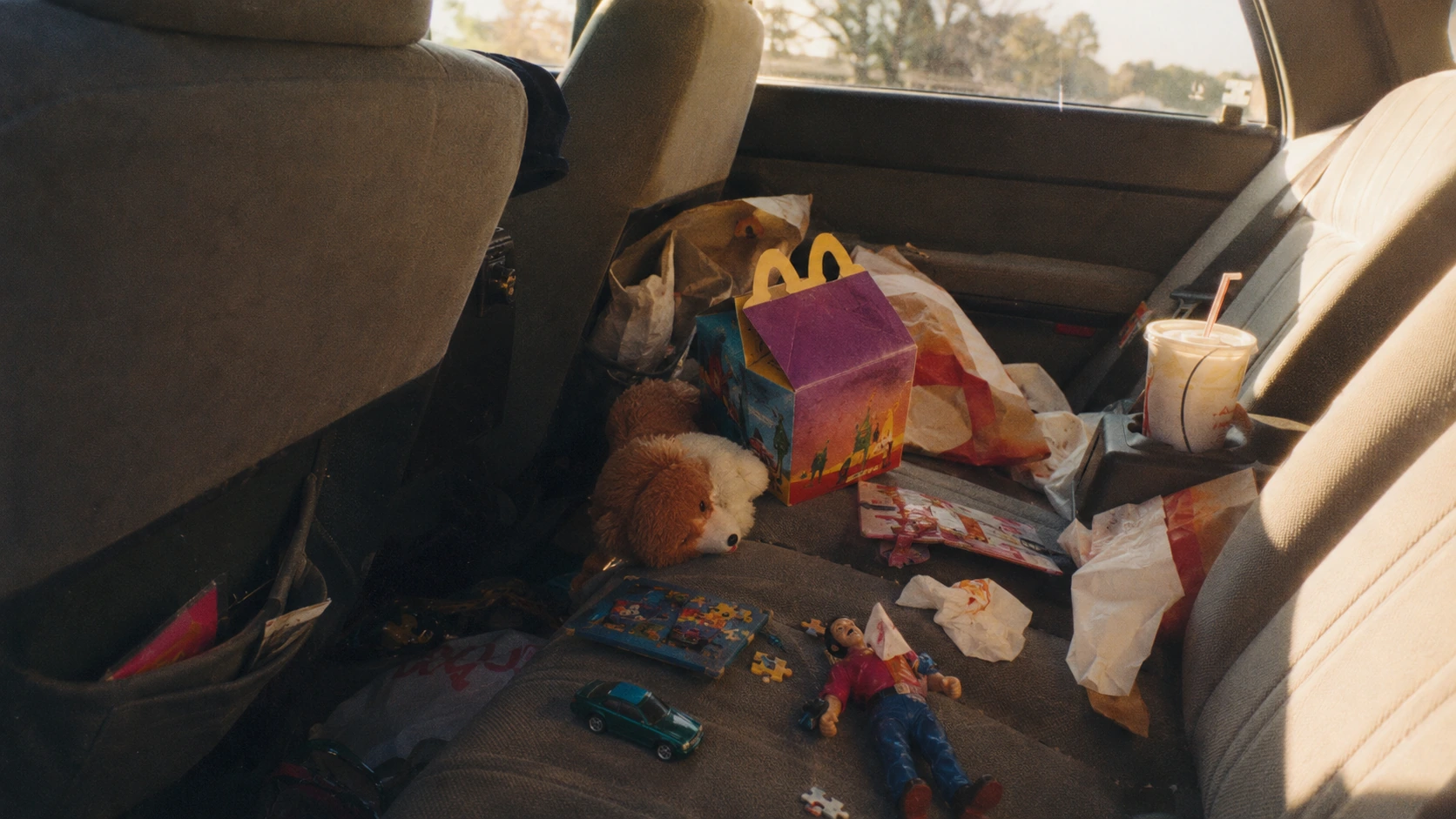 1990s family car back seat filled with fast-food wrappers, kids-meal toys and a meal box
