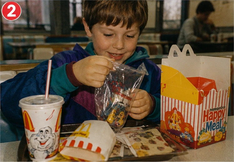 Child opening a 1990s kids-meal toy bag at a retro fast-food restaurant booth