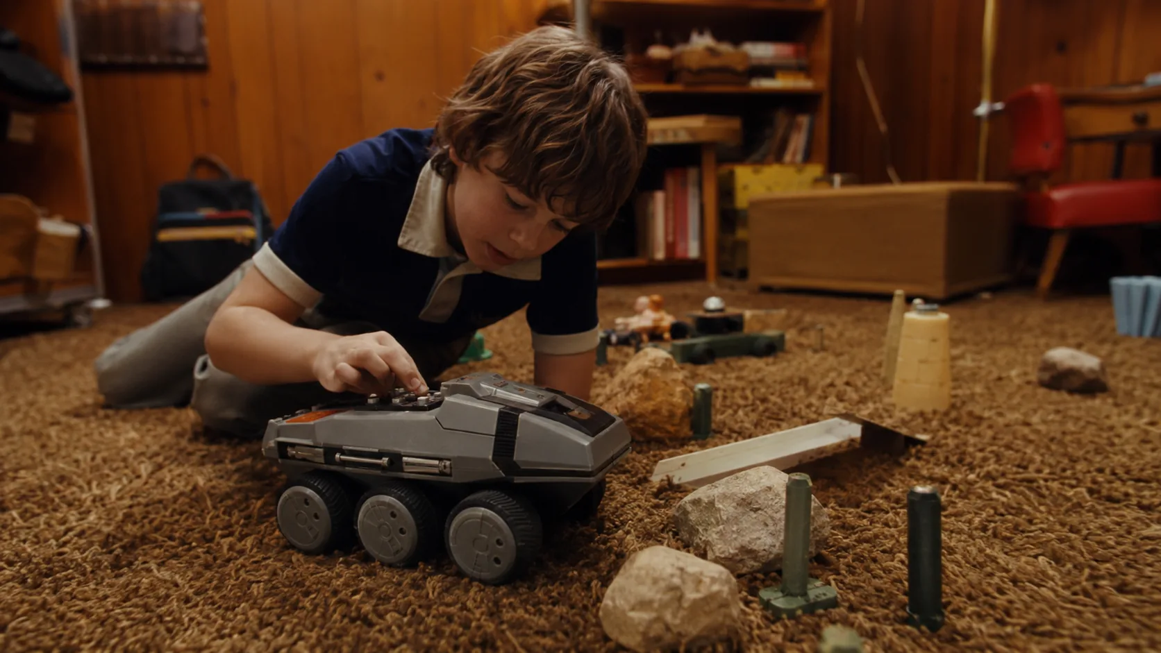 A child programming a Big Trak electronic vehicle across a 1970s shag-carpet playroom