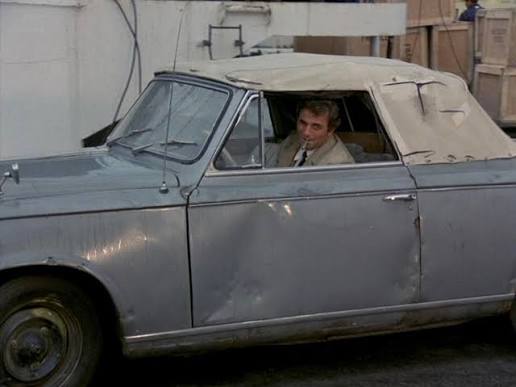 Lieutenant Columbo standing beside his battered Peugeot detective car