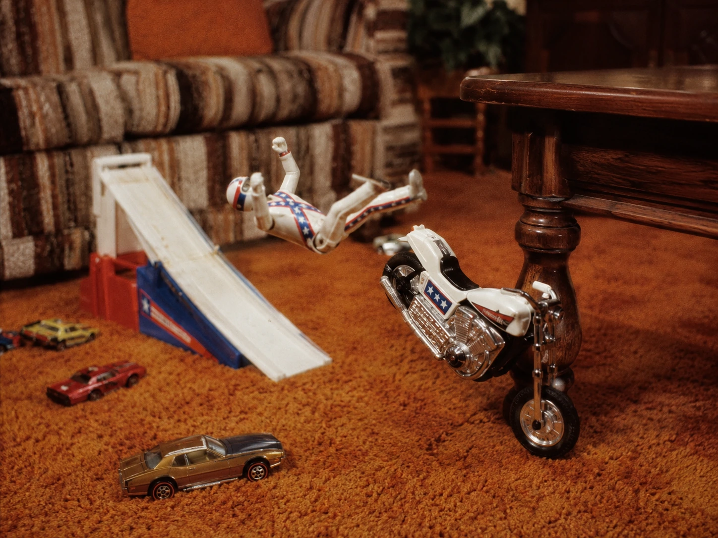 Evel Knievel toy motorcycle and rider tumbling toward a wooden coffee-table leg
