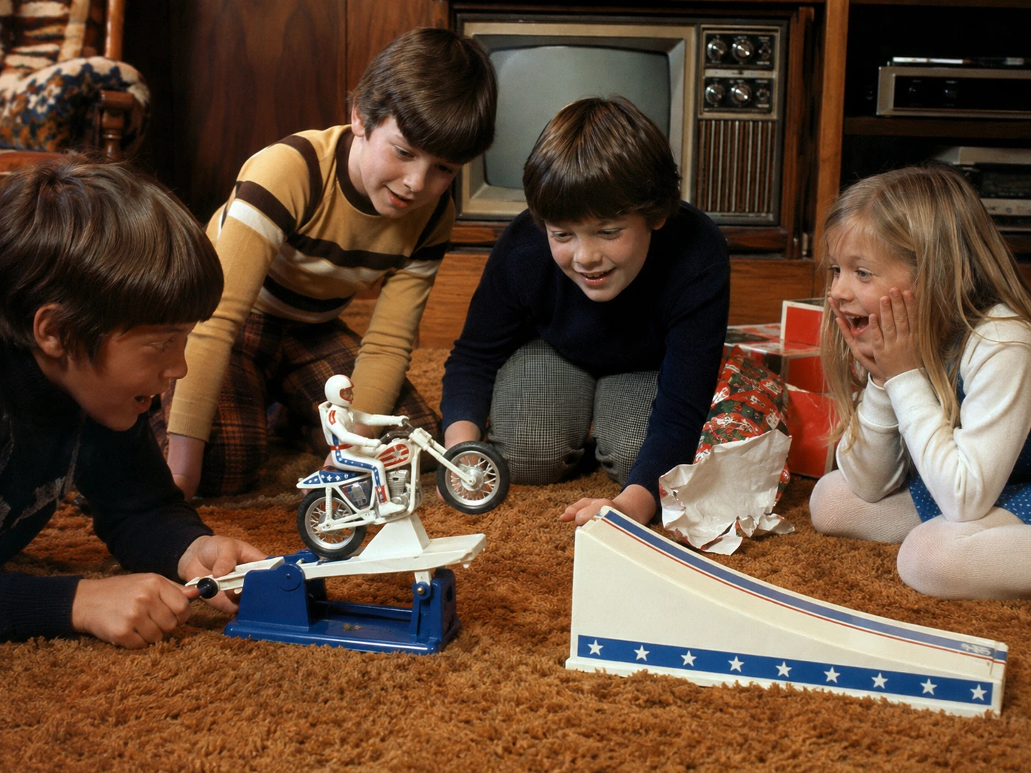 Children gathering around a newly opened Evel Knievel Stunt Cycle set in a 1970s living room