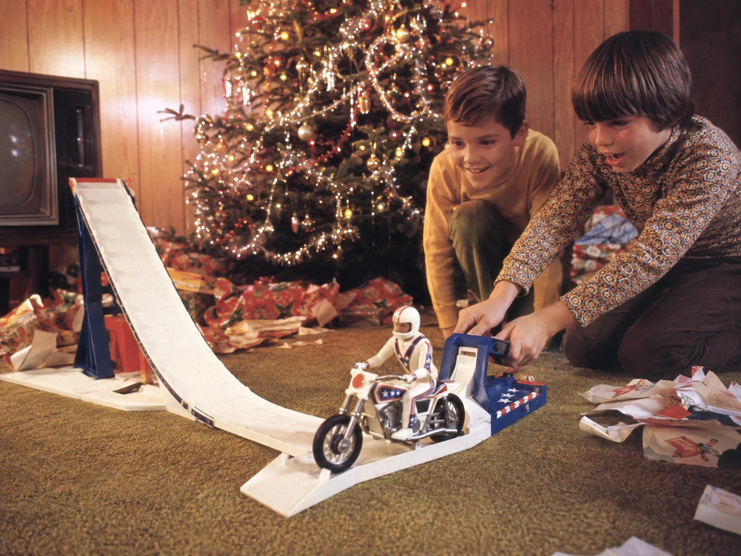 Children launching an Evel Knievel Stunt Cycle beside a decorated 1970s Christmas tree