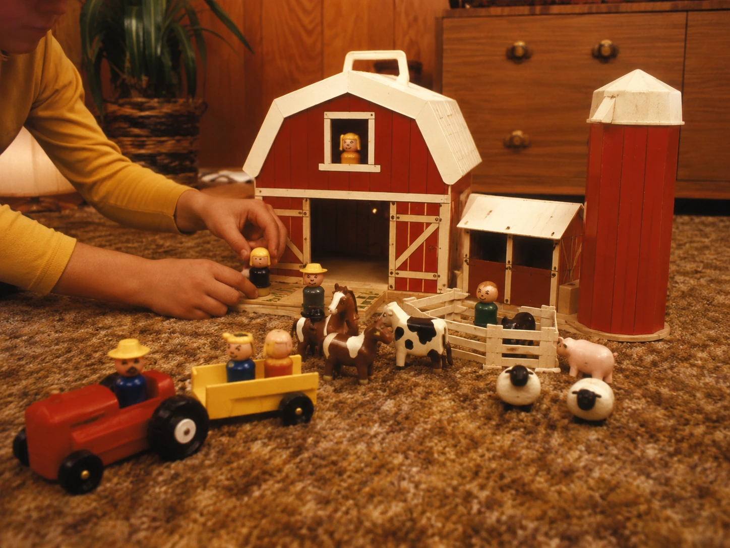 Child arranging farmers, animals and a tractor around a classic red Play Family Farm
