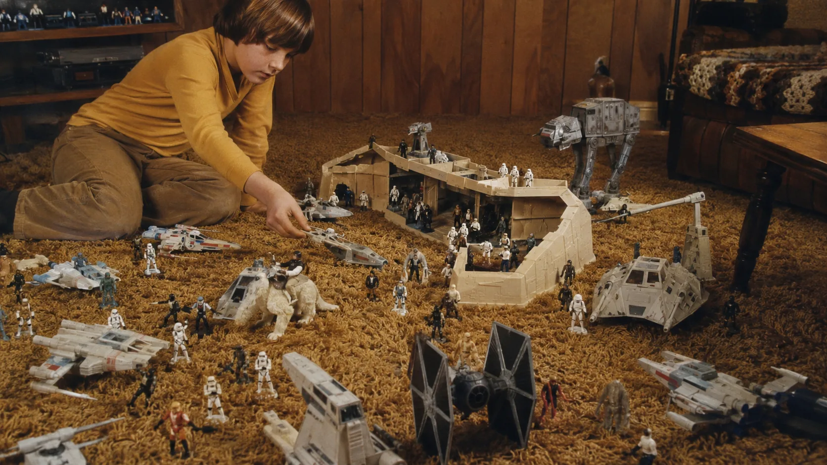 Child staging a Kenner Star Wars action-figure battle with small figures, spacecraft and a cardboard base on shag carpet