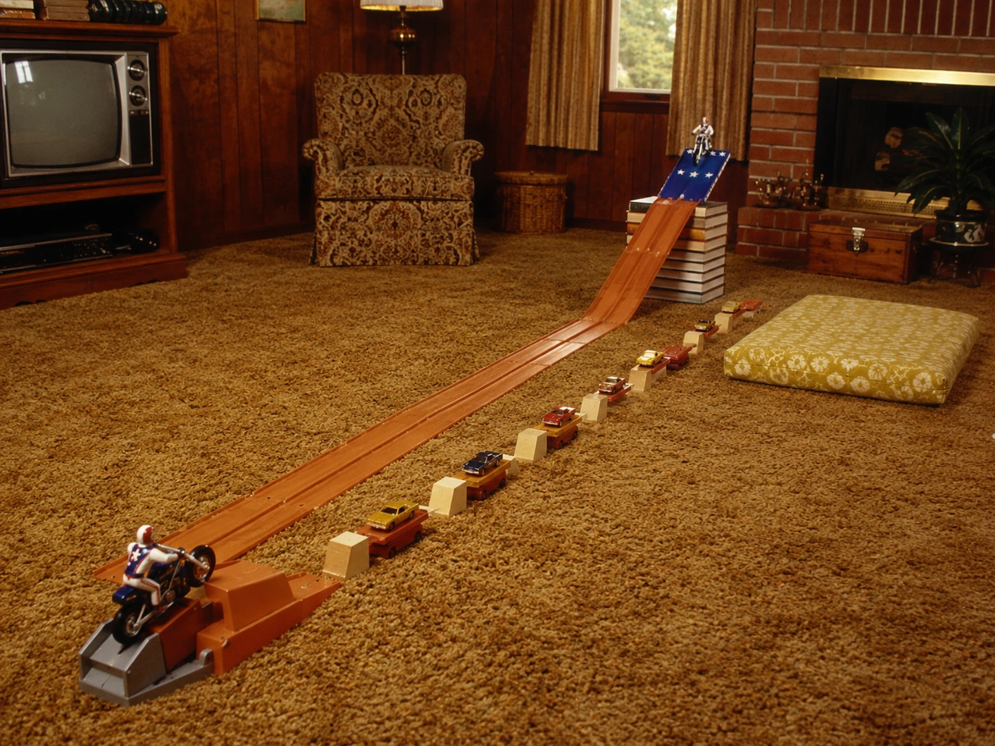 Long Evel Knievel stunt setup with launcher, runway, book ramp, toy-car obstacles and landing area