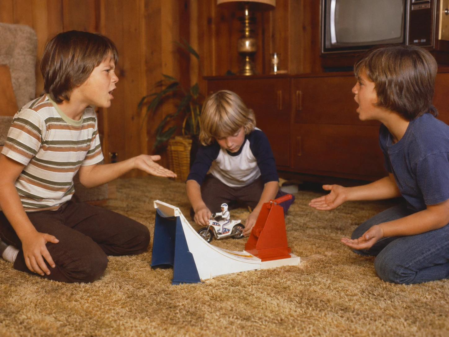 Three children arguing over turns with an Evel Knievel launcher and ramp