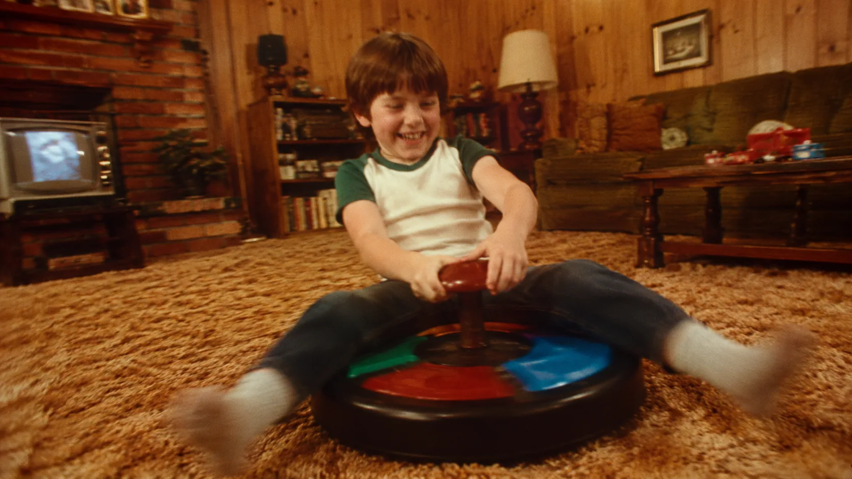 A child spinning on a Sit 'n Spin in a wood-paneled 1970s family room