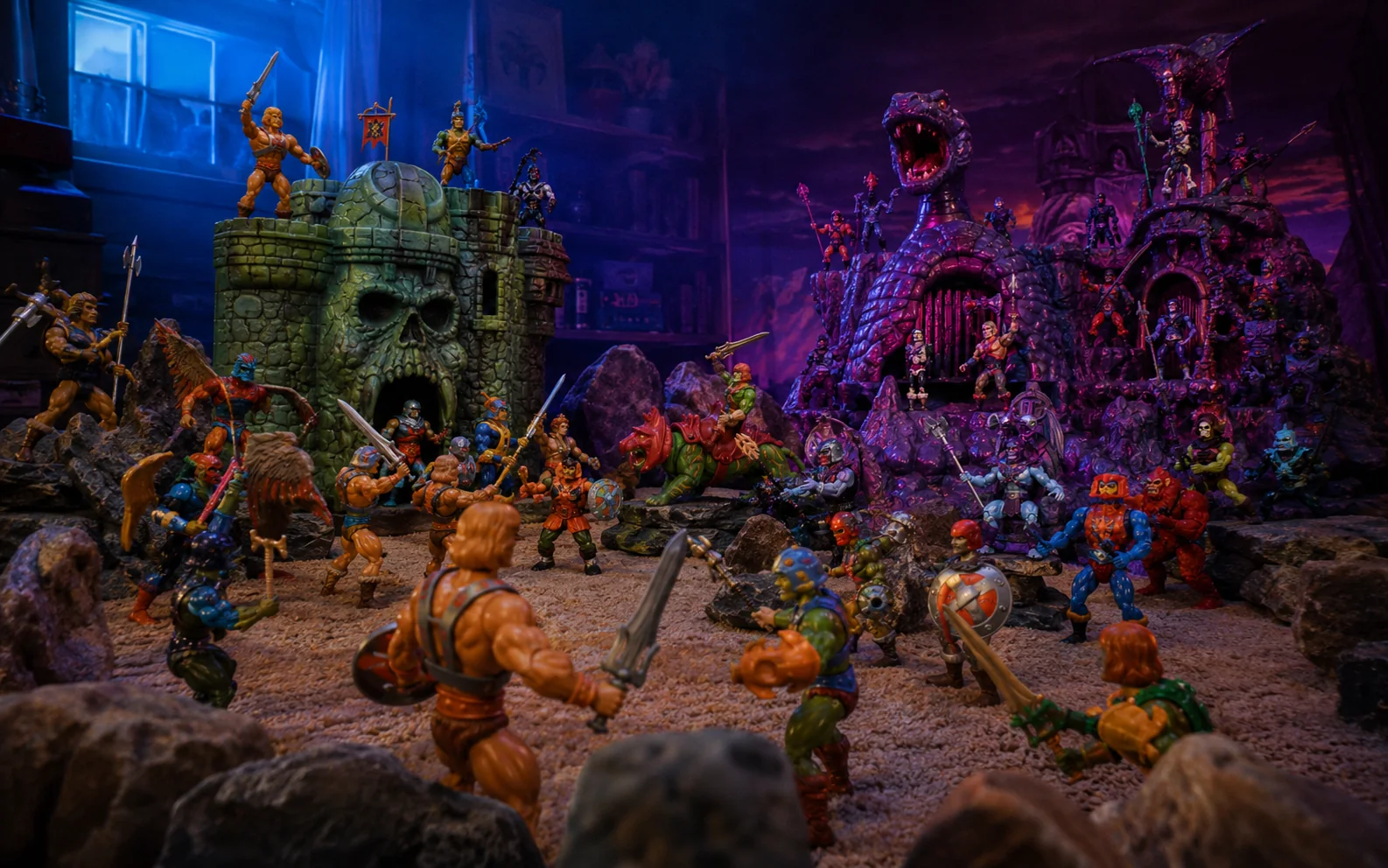Green skull-faced castle and purple serpent mountain playsets facing each other across a crowded 1980s fantasy action-figure battlefield.