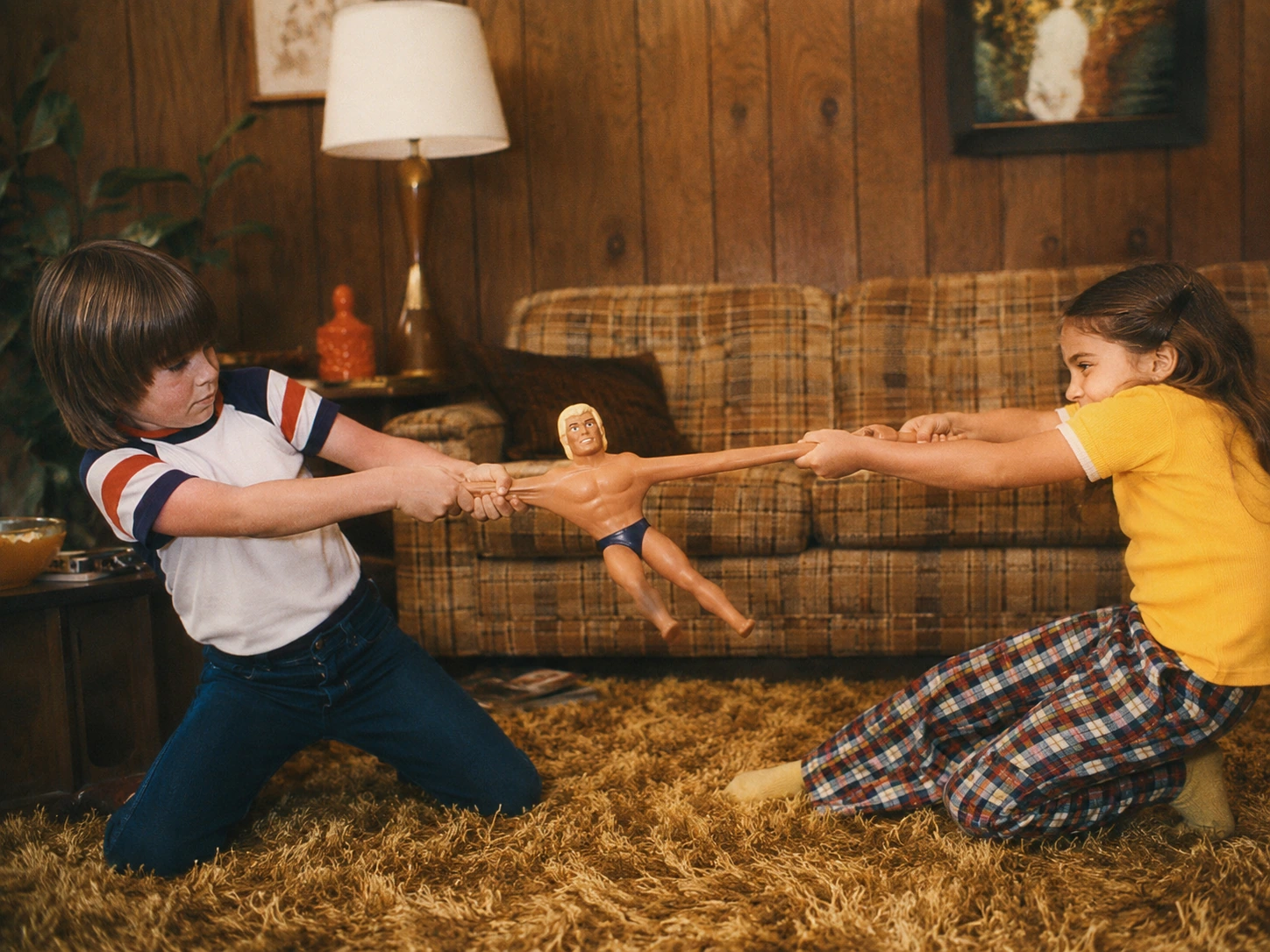 Two children pulling an original-style Stretch Armstrong across a wood-paneled 1970s living room