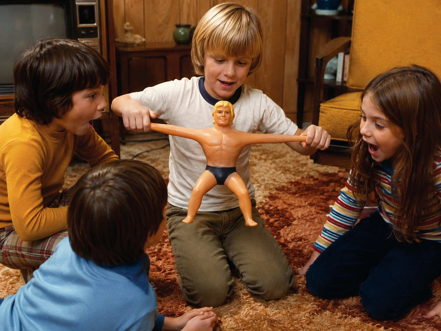 Children reacting as one child demonstrates Stretch Armstrong in a 1970s family room