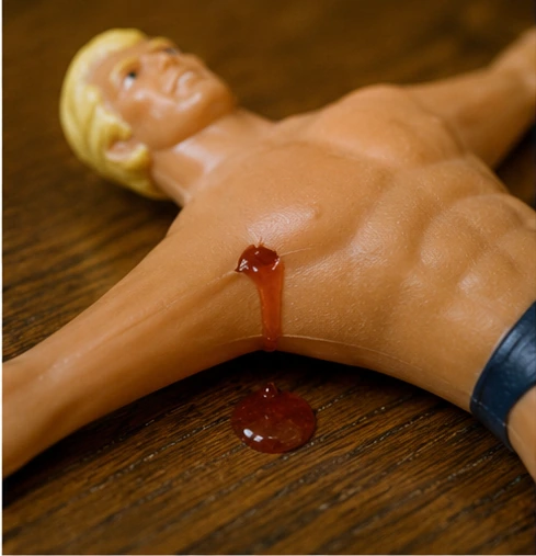Small puncture in Stretch Armstrong with a bead of thick red gel appearing on the skin