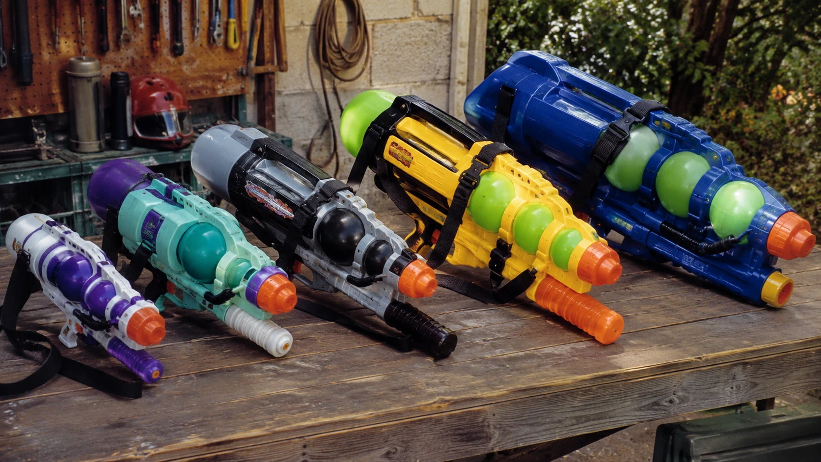 Large late-90s-style water blasters with multiple pressure chambers and straps displayed on a workshop table